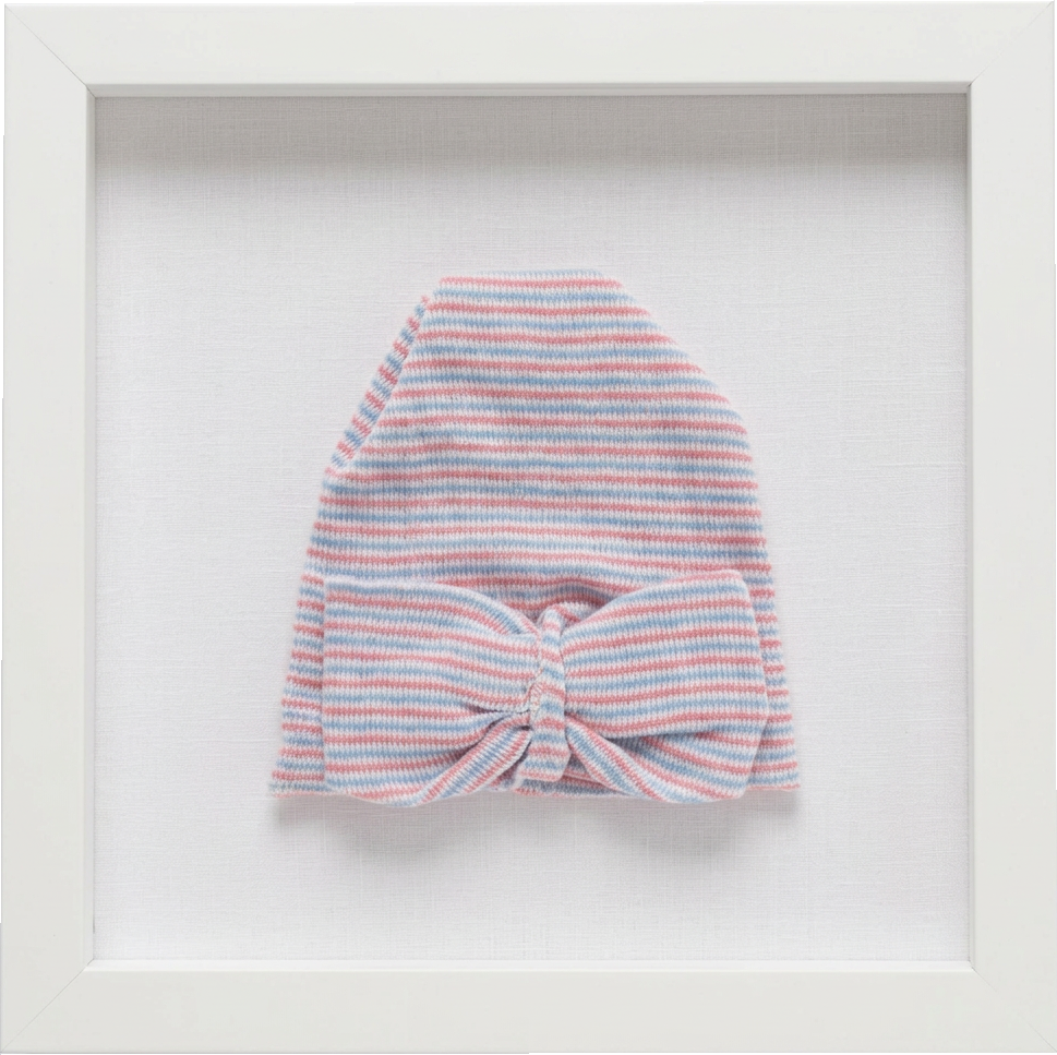 A first hat: A newborn’s hat floated on linen in a white shadow box.