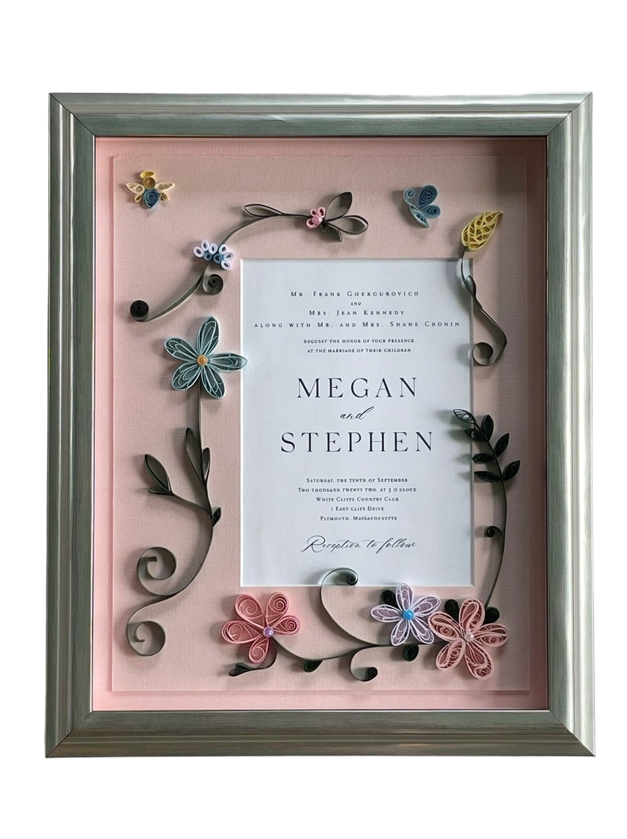 A wedding invitation: Quilled paper flowers on a blush mat, in a silver shadow box.
